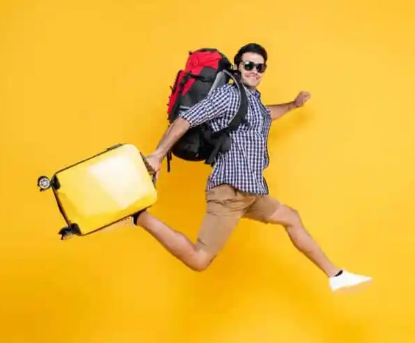 Afbeelding met vrolijke man met zonnebril op, backpack op zijn rug en gele koffer in zijn hand. 