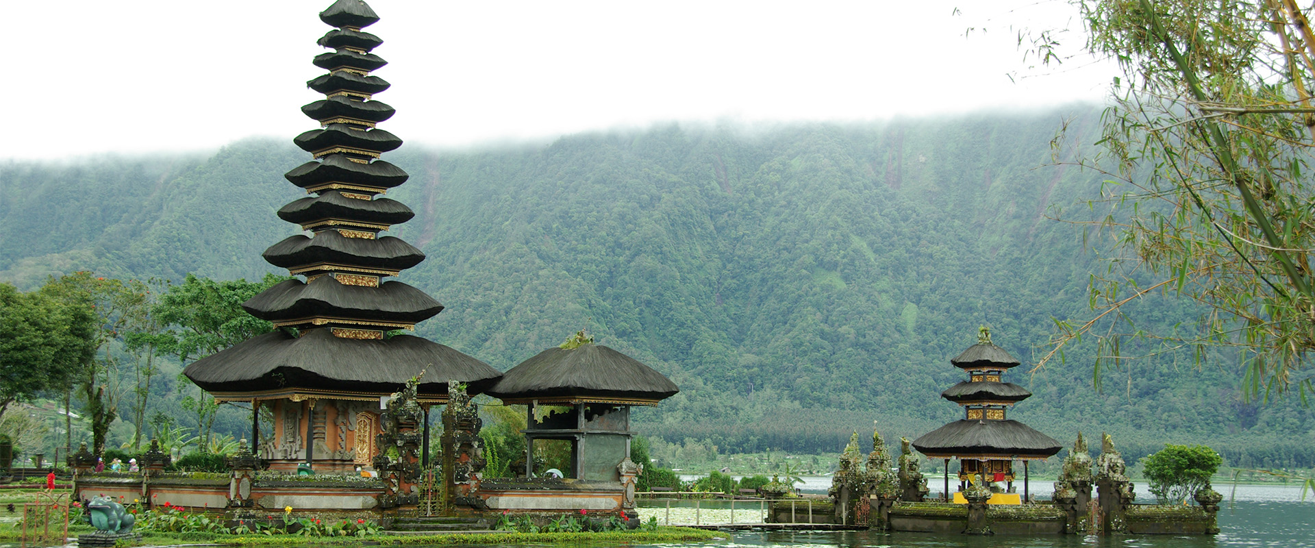 Afbeeldingen van tempel aan het water in Azië. Voorde tempel staan bloemen en op de achtergrond een heuvel met bomen. 